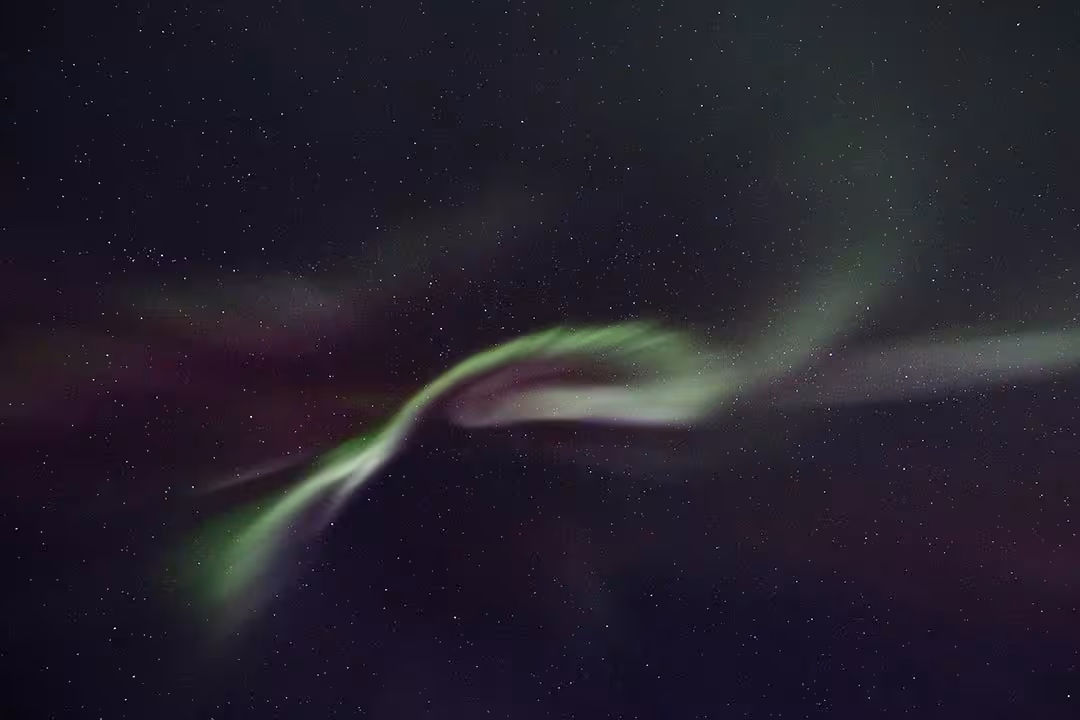 Aurora borealis ribbon glowing across a clear, star-filled night sky, ideal Northern Lights stargazing trip