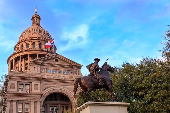 Bronze equestrian statue in front of the Texas State Capitol dome with American and Texas flags in Austin