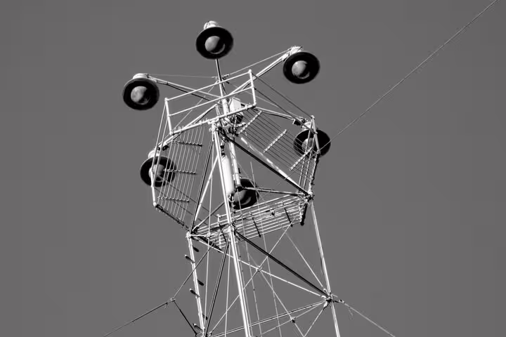 Tall metal tower with large speakers mounted on lattice structure against gray sky