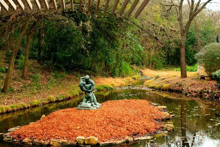Bronze sculpture on leaf-covered island in a tranquil creek surrounded by trees in Austin park