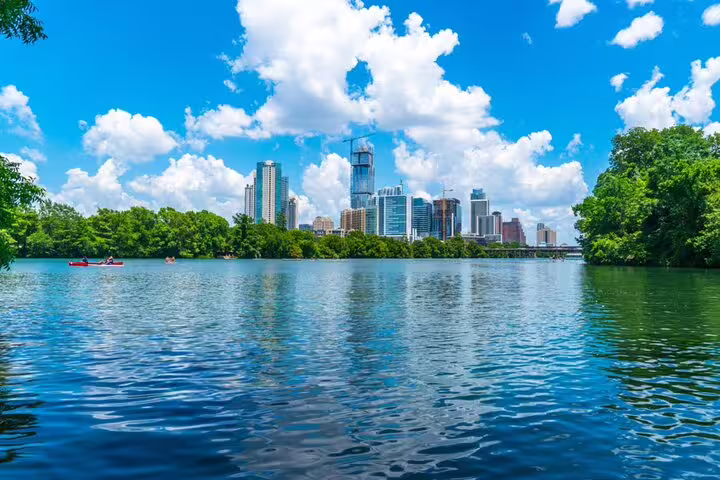 Austin skyline viewed from Lady Bird Lake with kayakers on calm blue water and lush green trees