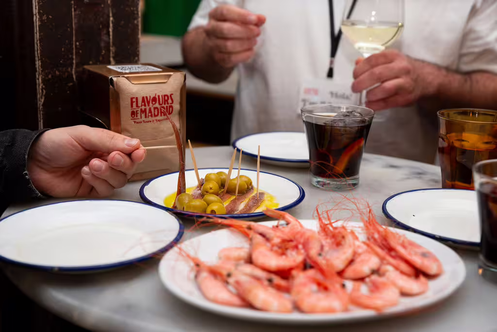 Authentic Madrid food tour with wine tasting, featuring tapas like olives and prawns, showcasing local Spanish culinary delights.