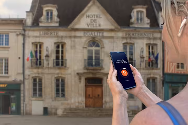 Visitor using audio guide app on smartphone in front of Auxerre Hôtel de Ville
