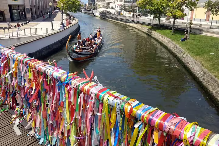 Colorful ribbons adorn a bridge over Aveiro's canal with a traditional boat, part of the Porto Aveiro Paiva Walkways tour.