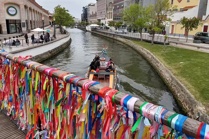 A vibrant bridge adorned with ribbons crosses Aveiro's canal, with a moliceiro boat navigating the serene waters.