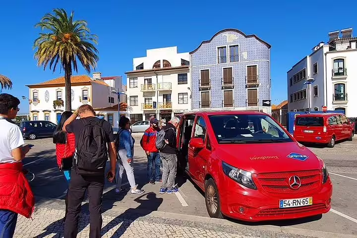 Tour group gathers near a red tour van in a picturesque Aveiro square with traditional Portuguese buildings.