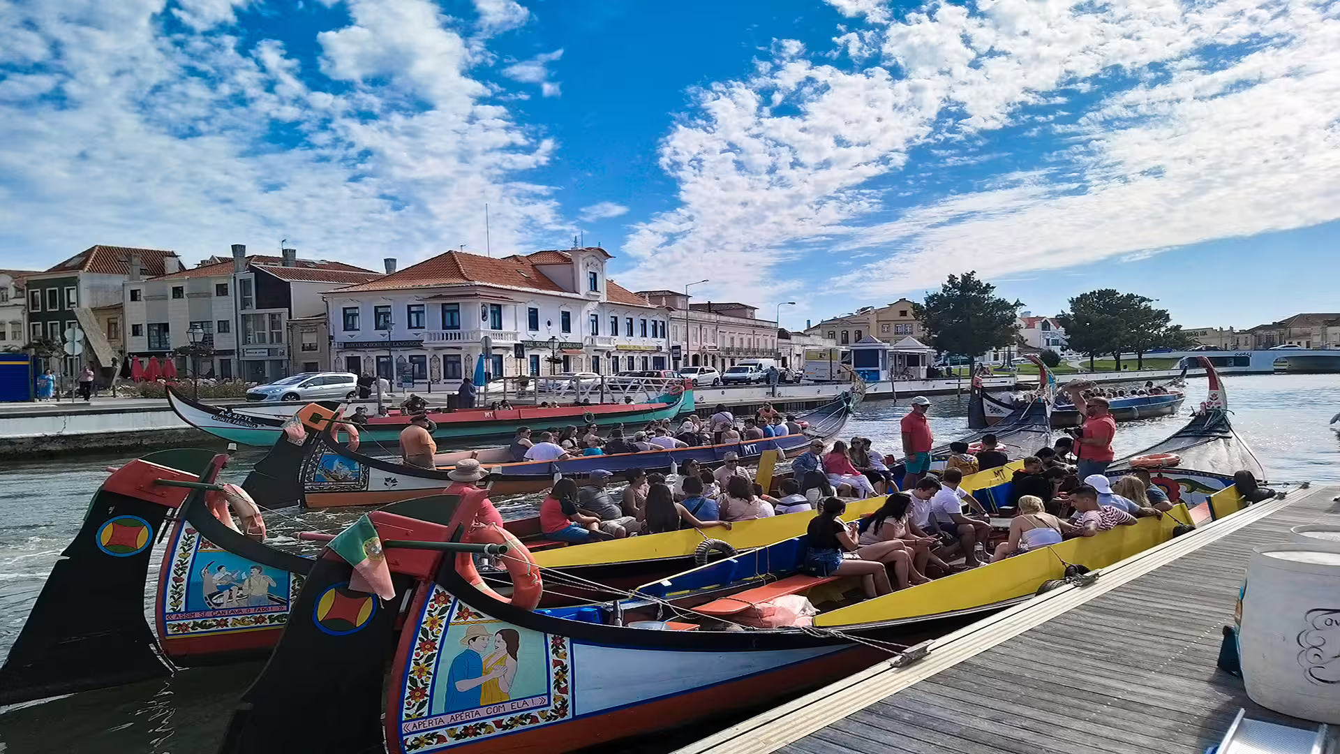 Colorful gondolas filled with tourists navigate the scenic canals of Aveiro, with charming coastal architecture in the background.