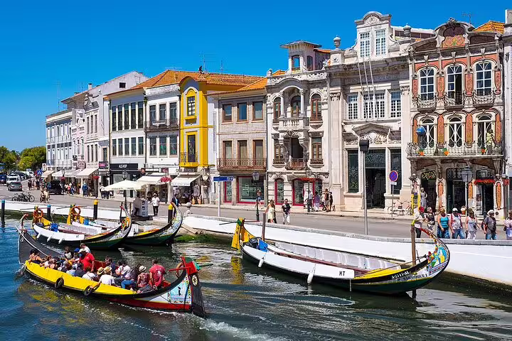 Colorful gondolas float along a canal in Aveiro, showcasing the vibrant architecture and lively atmosphere on the Porto to Lisbon private journey.