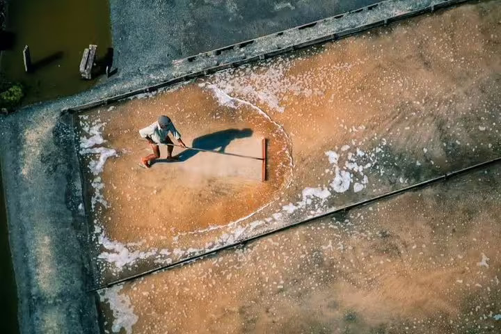 Aerial view of a worker harvesting salt in traditional salt pans in Aveiro, showcasing local culture on a full-day tour.