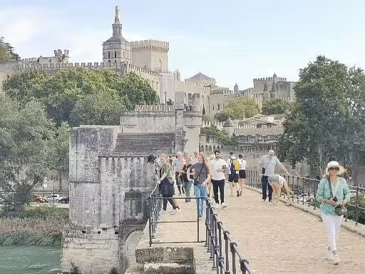 Walk across Avignon bridge toward the Palais des Papes, key site on an 11-day Christian heritage tour in Provence
