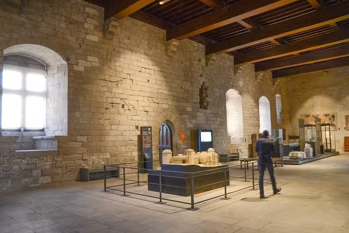 Interior of Avignon Papal Palace museum hall with stone walls, arched windows, and architectural scale model display