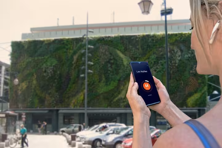 Woman holding smartphone with audio guide app at Les Halles green wall in Avignon