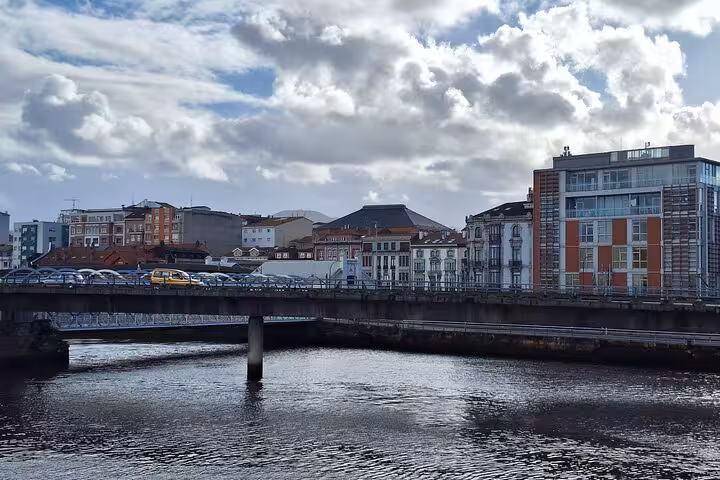Scenic view of Aviles with a bridge over the river, showcasing colorful buildings under a partly cloudy sky.
