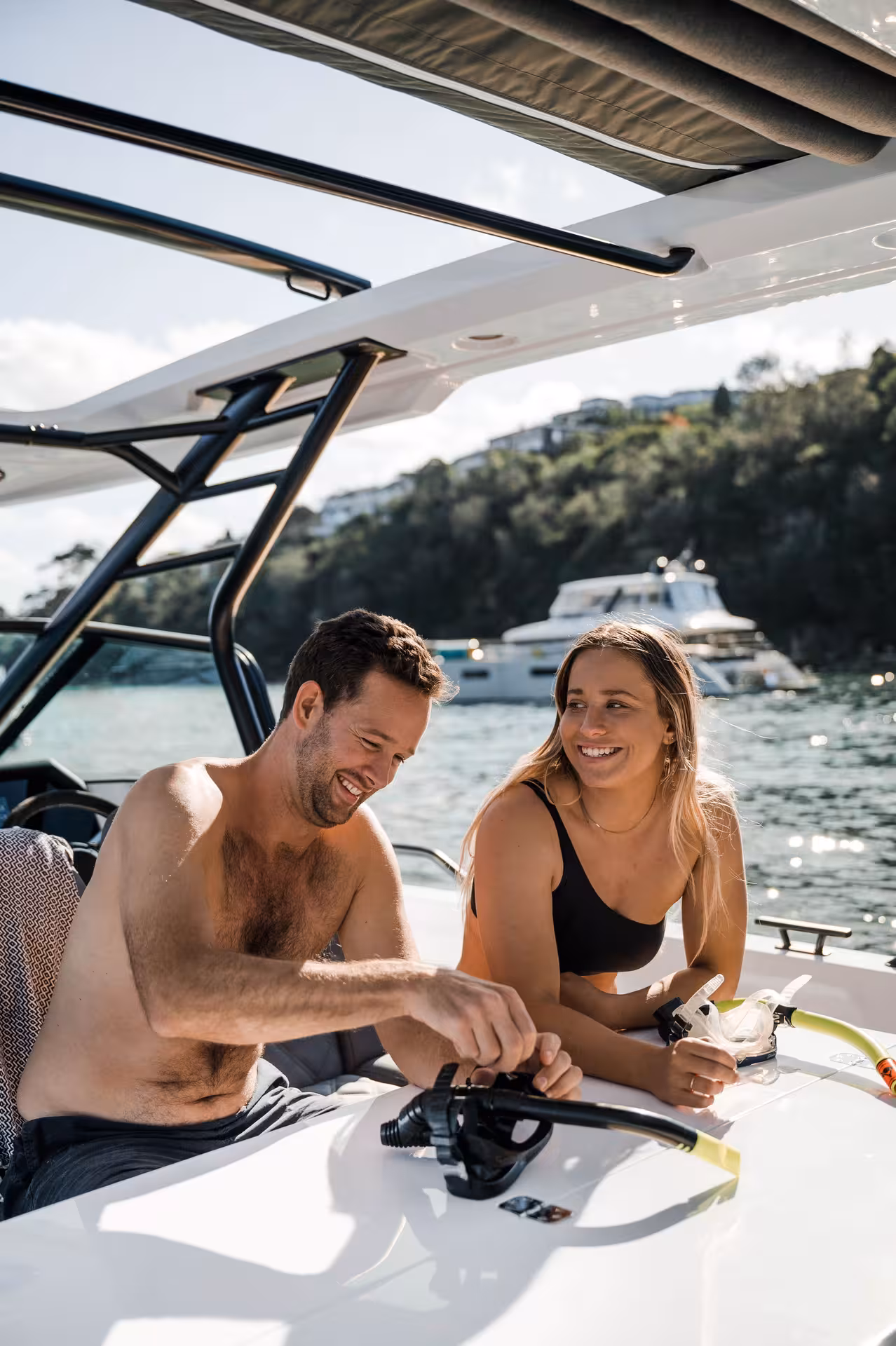 Couple preparing snorkel gear on an Axopar 25 CT half-day rental, anchored in a sunny bay near yachts