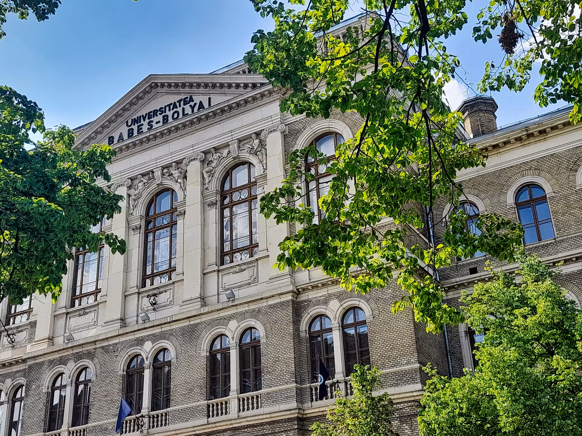 Historic Babes-Bolyai University neoclassical facade framed by lush trees on a guided walking tour in Cluj-Napoca
