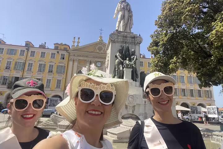 Three women smiling at bachelorette party selfie near statue in Nice Old Town square