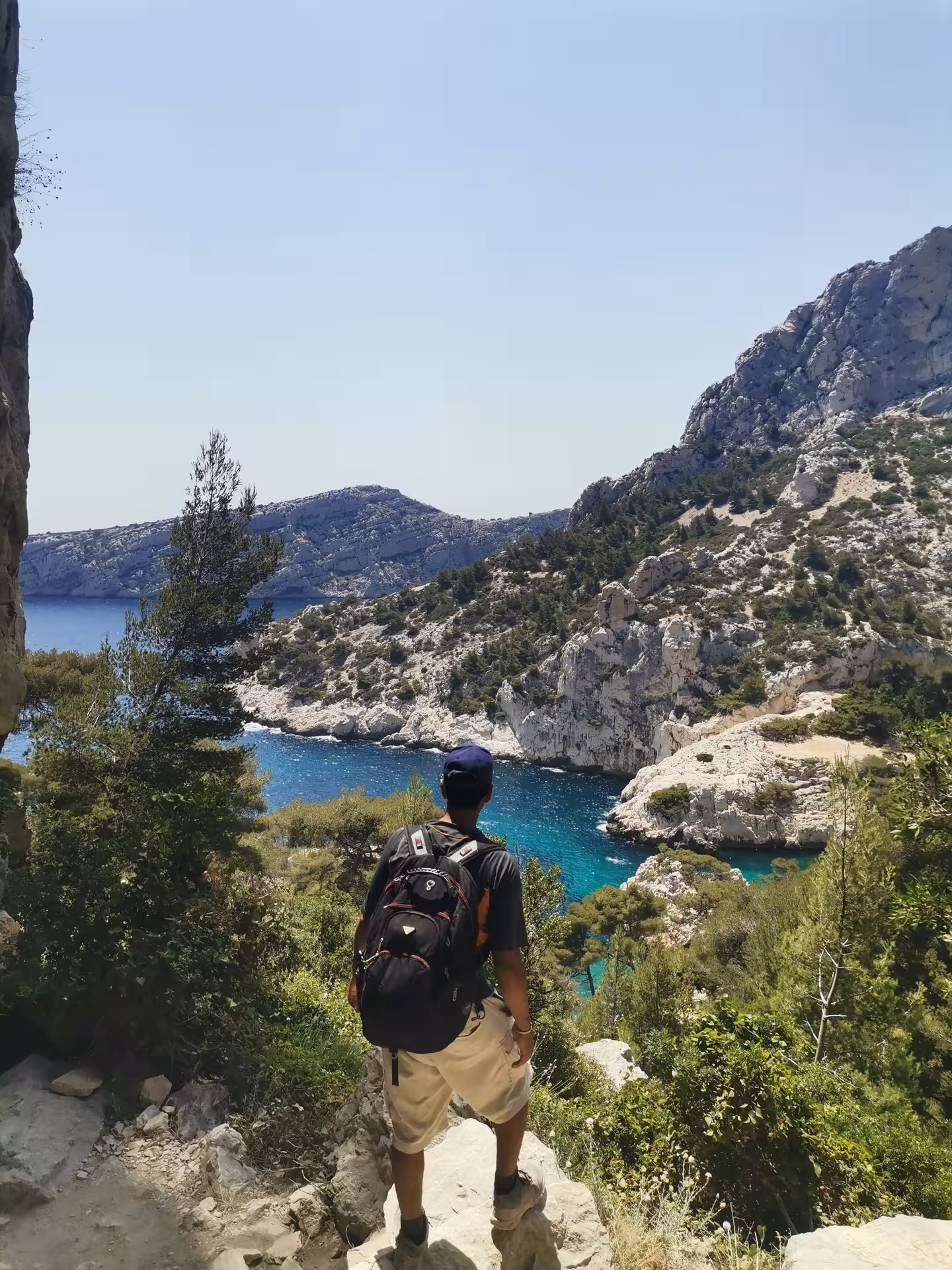 Backpacker overlooking bright blue Calanques inlet on Provence coastal hike, part of 7-day hiking getaway