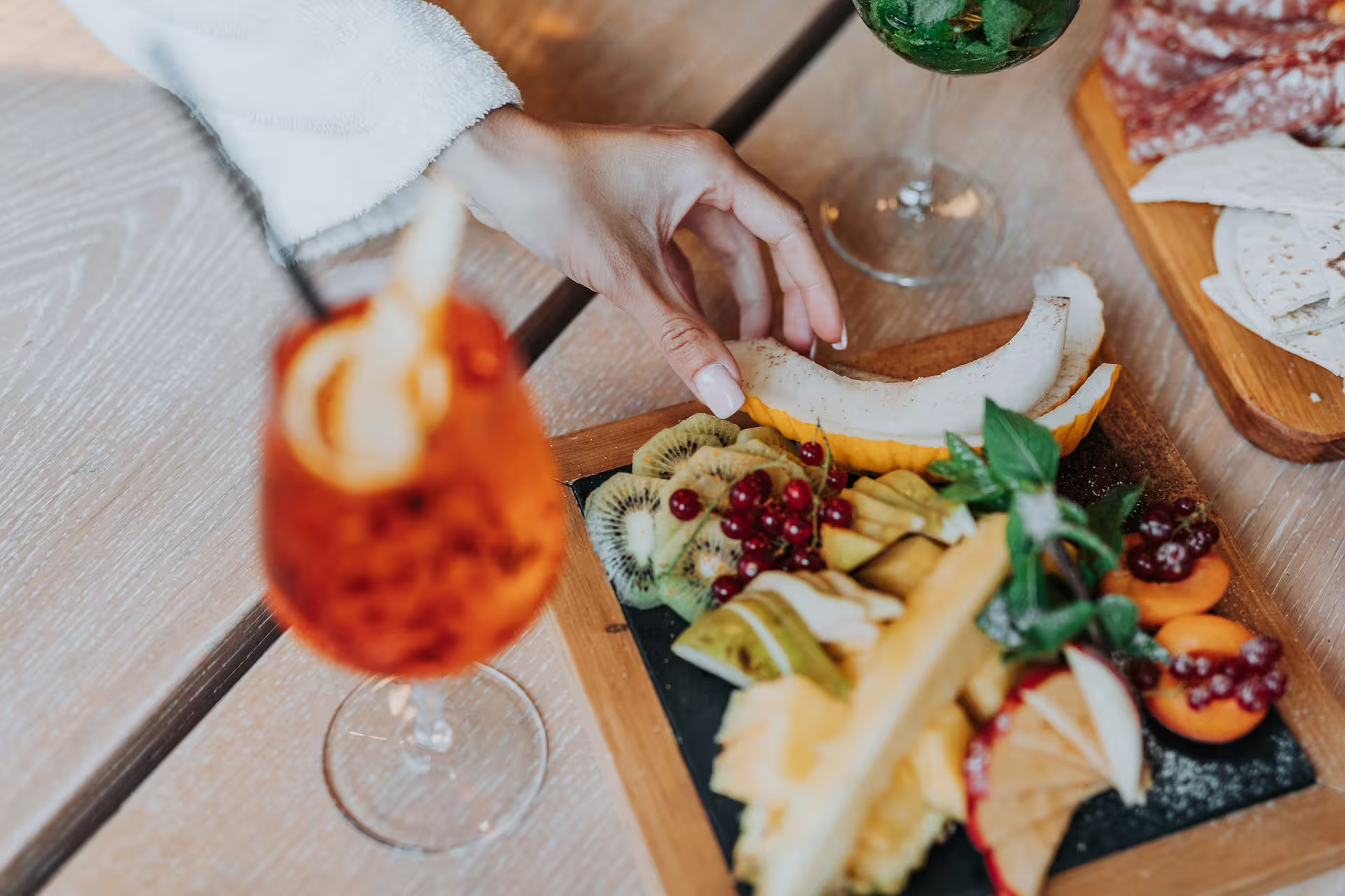 Hand reaching for fruit on aperitif board beside spritz, after Bagno di Romagna thermal pool session