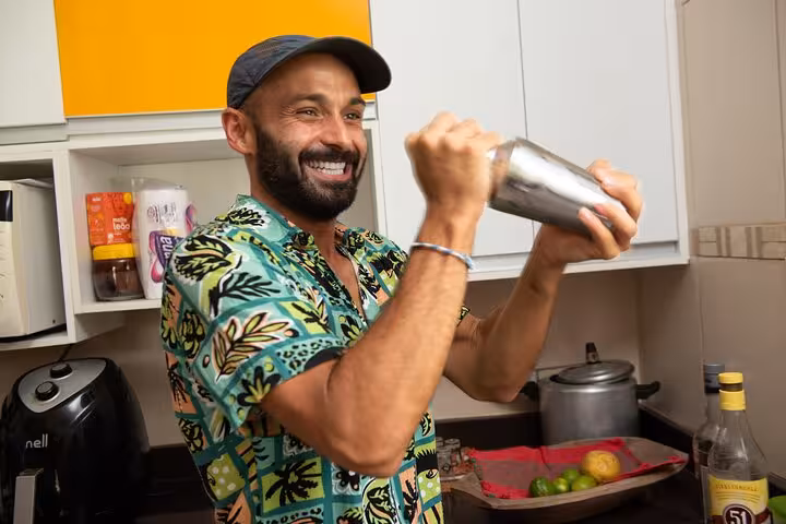 Smiling participant shaking a cocktail shaker during a boozy Bahian cooking class in Salvador's vibrant kitchen.