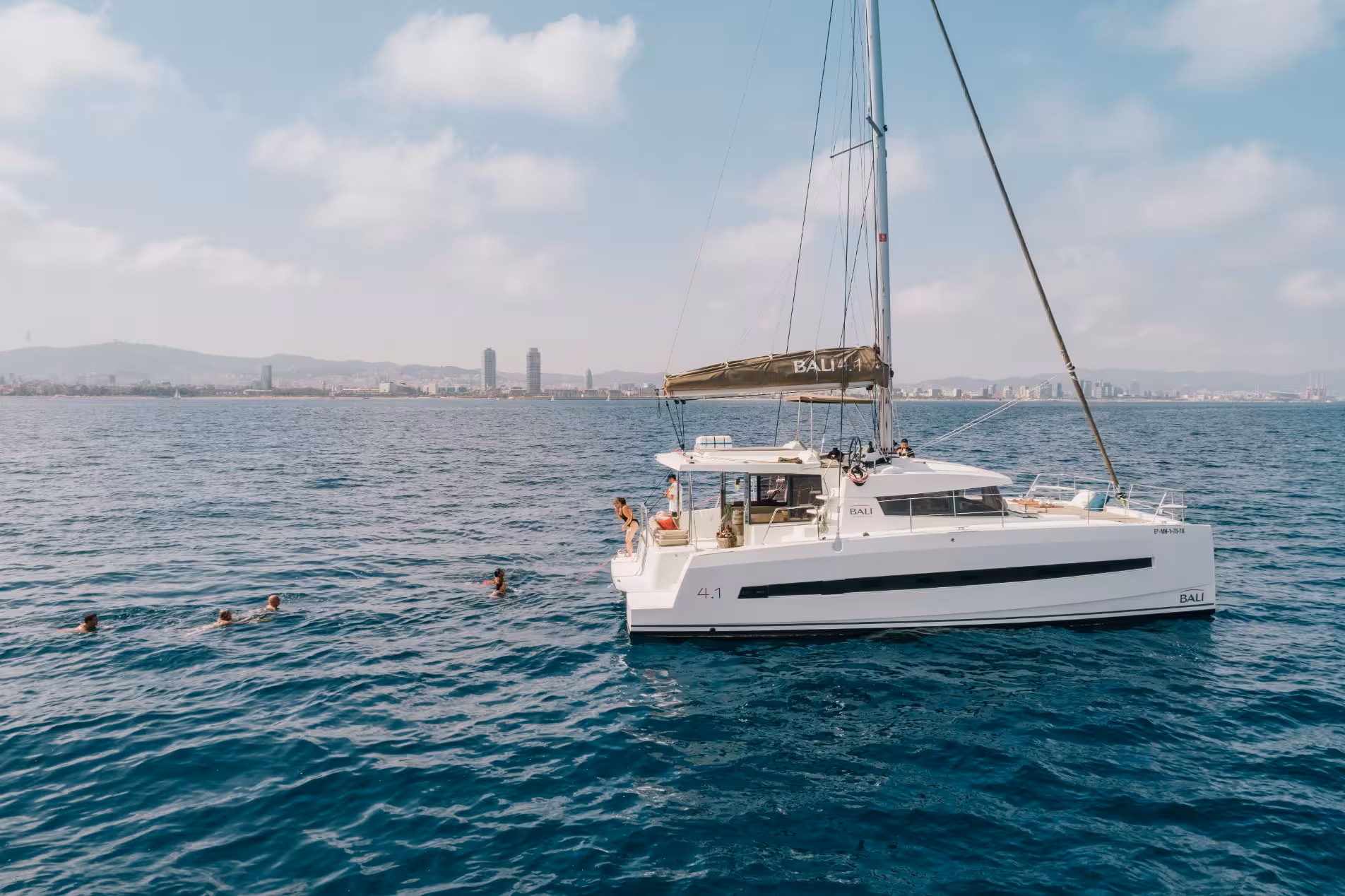 Bali 4.1 private luxury catamaran in Barcelona with guests swimming in the Mediterranean near the city skyline