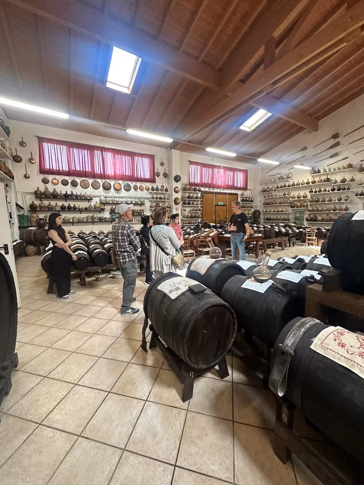 Tour group exploring a balsamic vinegar cellar, surrounded by aging barrels and traditional tools.