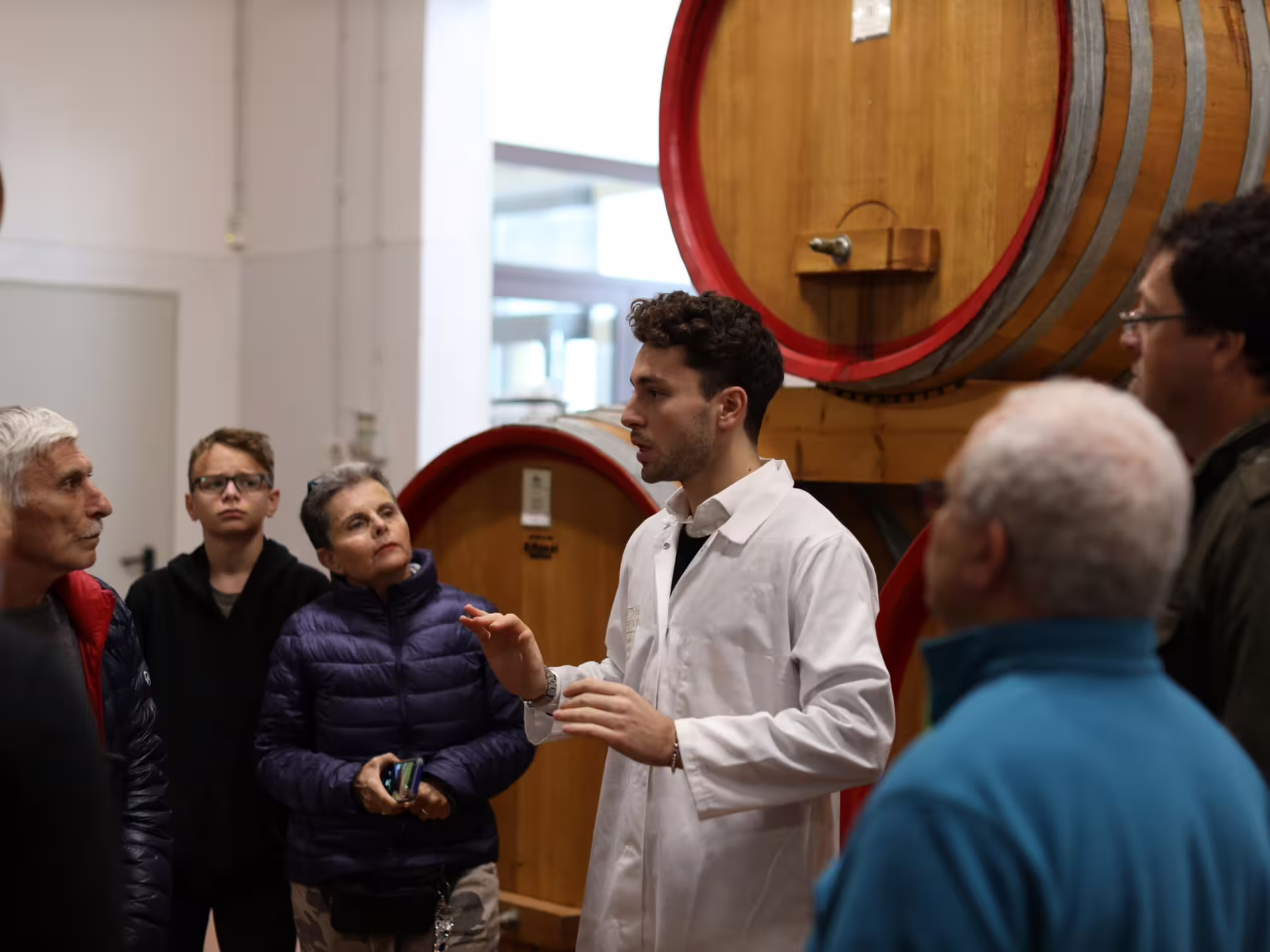 Guide explaining balsamic vinegar production to visitors beside large barrels on a Modena acetaia tour