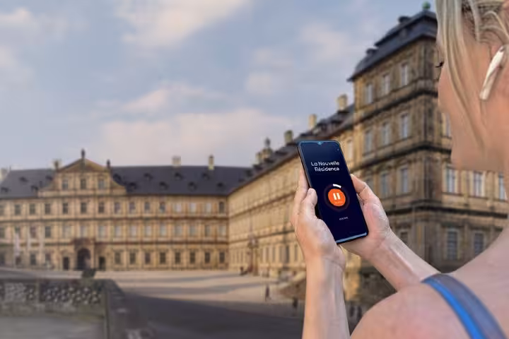 Tourist using self-guided audio tour app on smartphone in front of Bamberg New Residence palace
