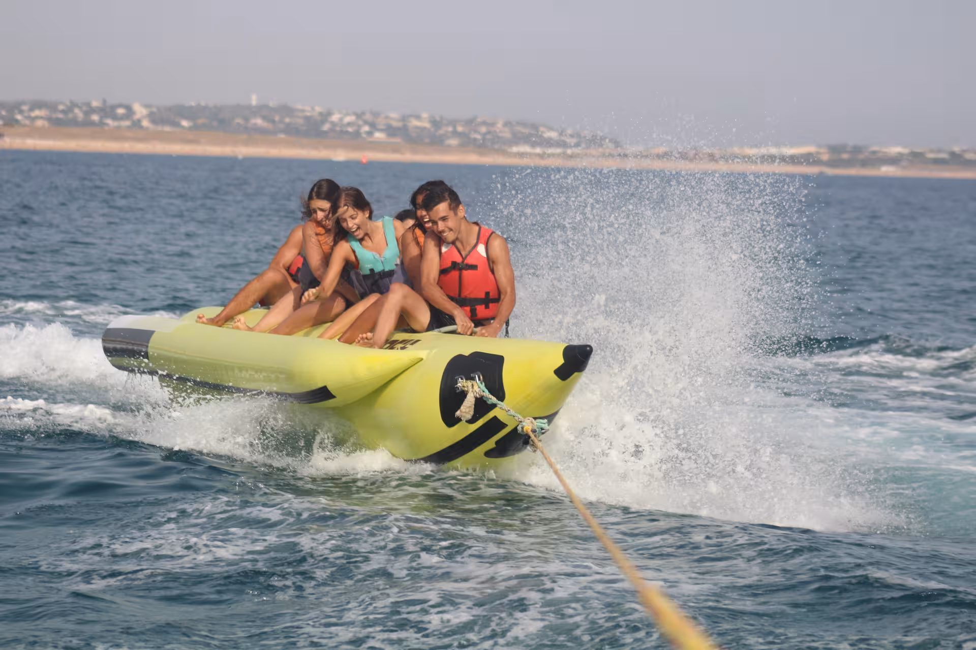 Thrilling banana boat ride in Armacao de Pera with excited riders splashing through ocean waves on a sunny day