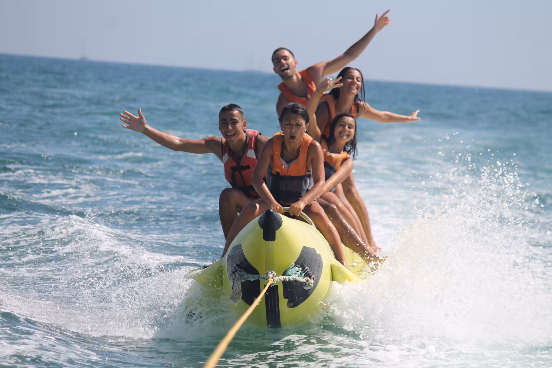 Excited group riding a yellow inflatable banana boat on sparkling ocean waters during a thrilling family boat tour in Armacao de Pera