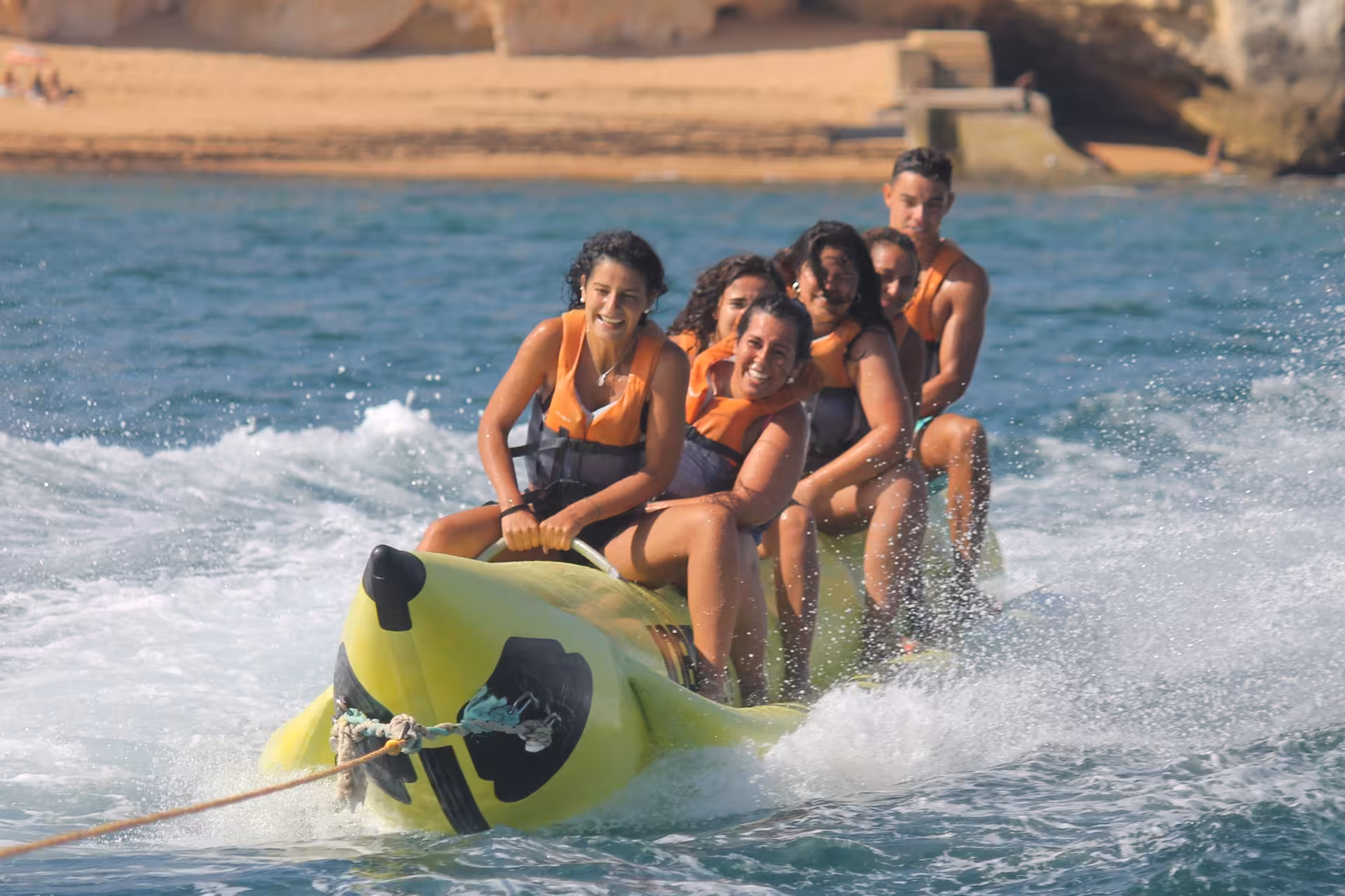 Smiling group in life jackets speeding on a yellow banana boat near scenic Armacao de Pera cliffs on a sunny family water sports tour