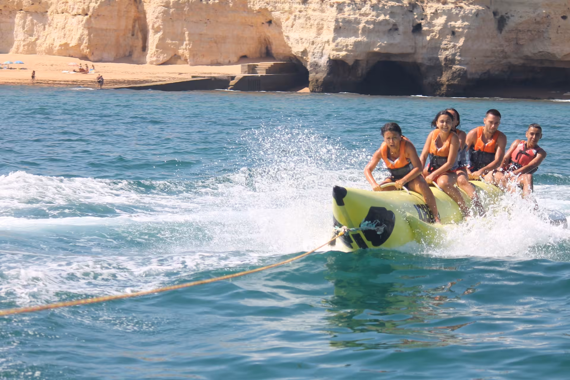 Group of riders on a yellow banana boat speeding past scenic Algarve cliffs during an exciting Armacao de Pera boat tour