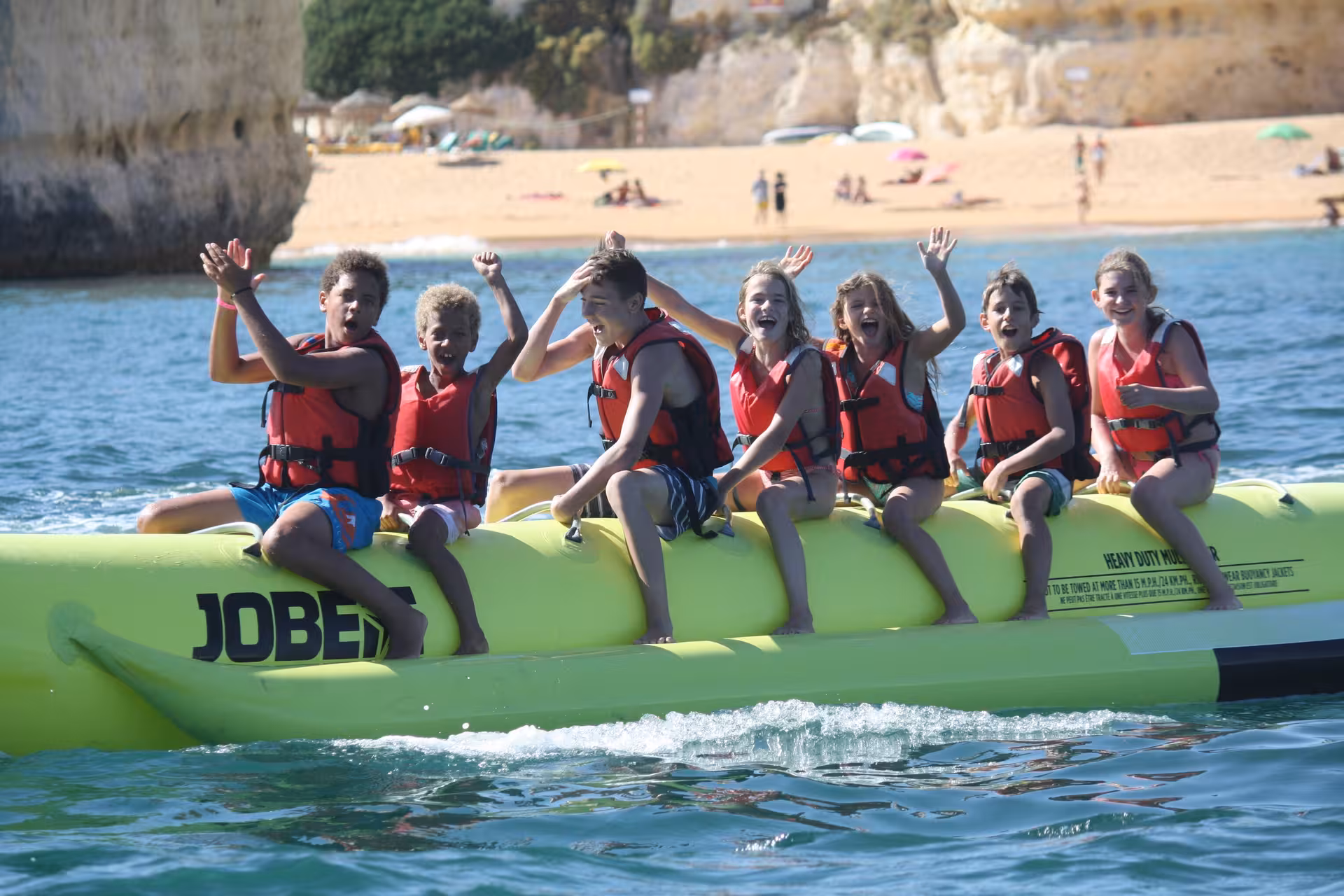 Excited kids in life jackets waving on a banana boat ride near Armacao de Pera beach Algarve Portugal