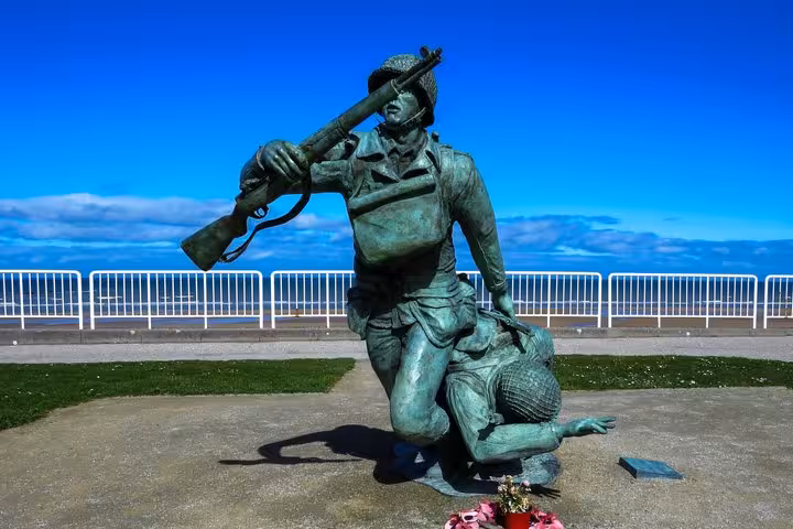 Bronze WWII soldier statue carrying rifle at Normandy D-Day memorial site with ocean backdrop