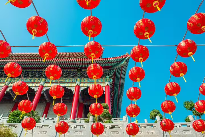 Red Chinese lanterns hanging above ornate temple gate in Bangkok Chinatown under blue sky