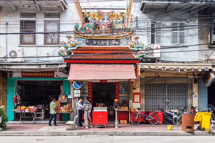 Colorful Chinese shrine temple facade on a Bangkok Chinatown street with locals and shophouses
