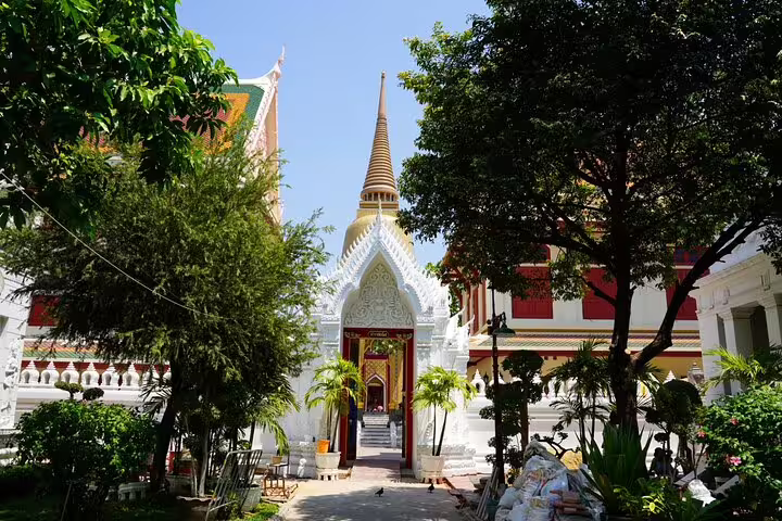 White Thai temple with golden spire and ornate gateway surrounded by trees in Bangkok old town