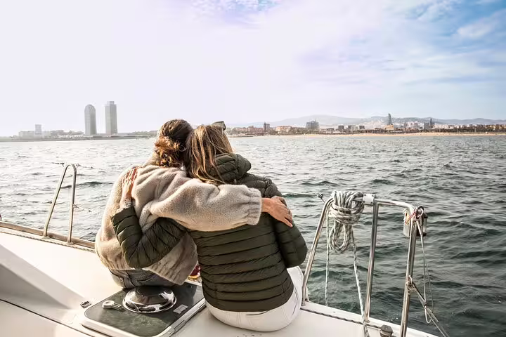Couple enjoying a private catamaran cruise with snacks and cava, overlooking Barcelona's skyline at sunset on the Mediterranean Sea.
