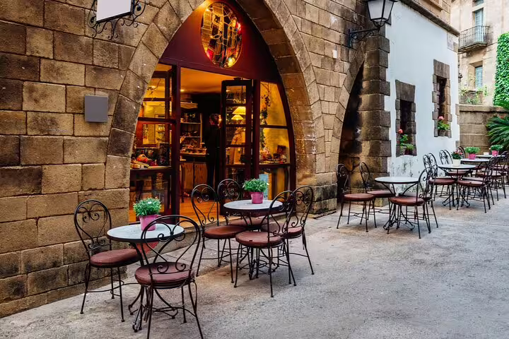 Charming outdoor cafe with wrought iron chairs and tables set against ancient stone arch in Barcelona's Gothic Quarter