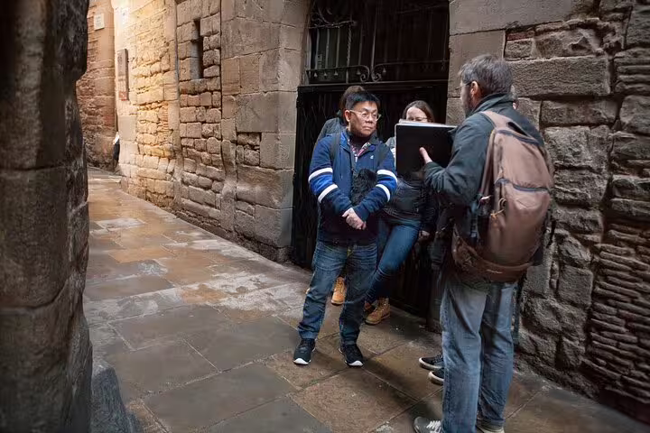 Tour guide explaining historical details to tourists in the ancient stone alley of Barcelona's Jewish Quarter.