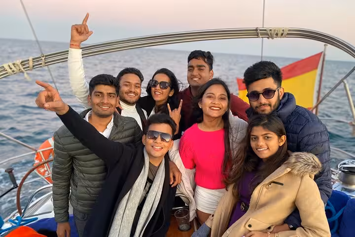 Group of friends smiling on a Barcelona private luxury sailing tour with Spanish flag and sea at sunset