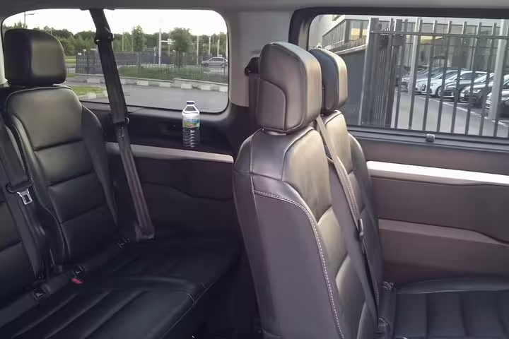 Spacious black leather rear seats inside a private chauffeur transfer vehicle with water bottle