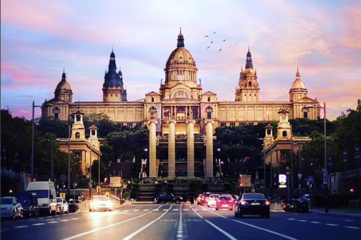 Evening view of Barcelona's National Palace with vibrant sky and bustling traffic, showcasing iconic architecture.