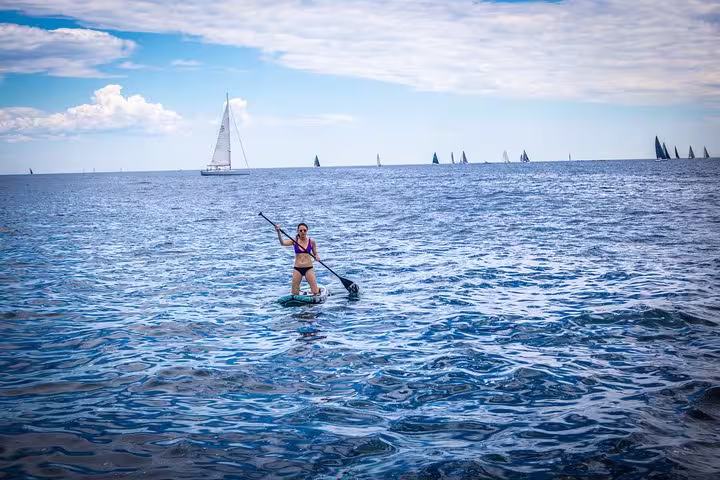 Woman paddleboarding in the blue waters of Barcelona with sailboats in the background during a private sailing tour.
