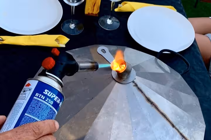 A chef uses a blowtorch on a traditional paella pan lid during a Barcelona cooking class experience.