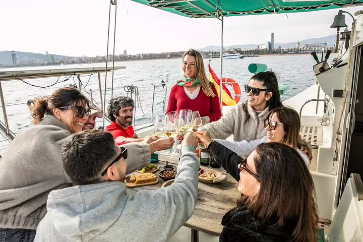 A group enjoys snacks and cava on a private catamaran tour in Barcelona, with a scenic city backdrop and sunset option available.