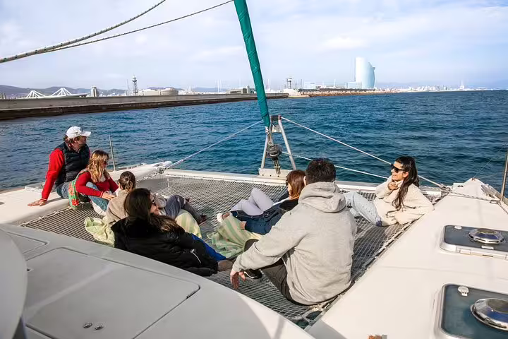 Group relaxing on a private catamaran in Barcelona, enjoying snacks and cava with a view of the sea and city skyline.