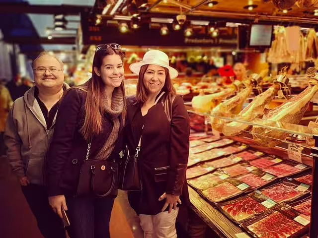 Tourists enjoying a private Barcelona highlights tour with tapa and drink, exploring a vibrant local market filled with cured meats.