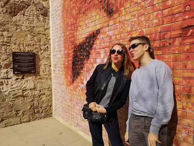 Tourists enjoying the vibrant El Beso de Joan Fontcuberta mural in Barcelona, part of a private tour with tapas and drinks.