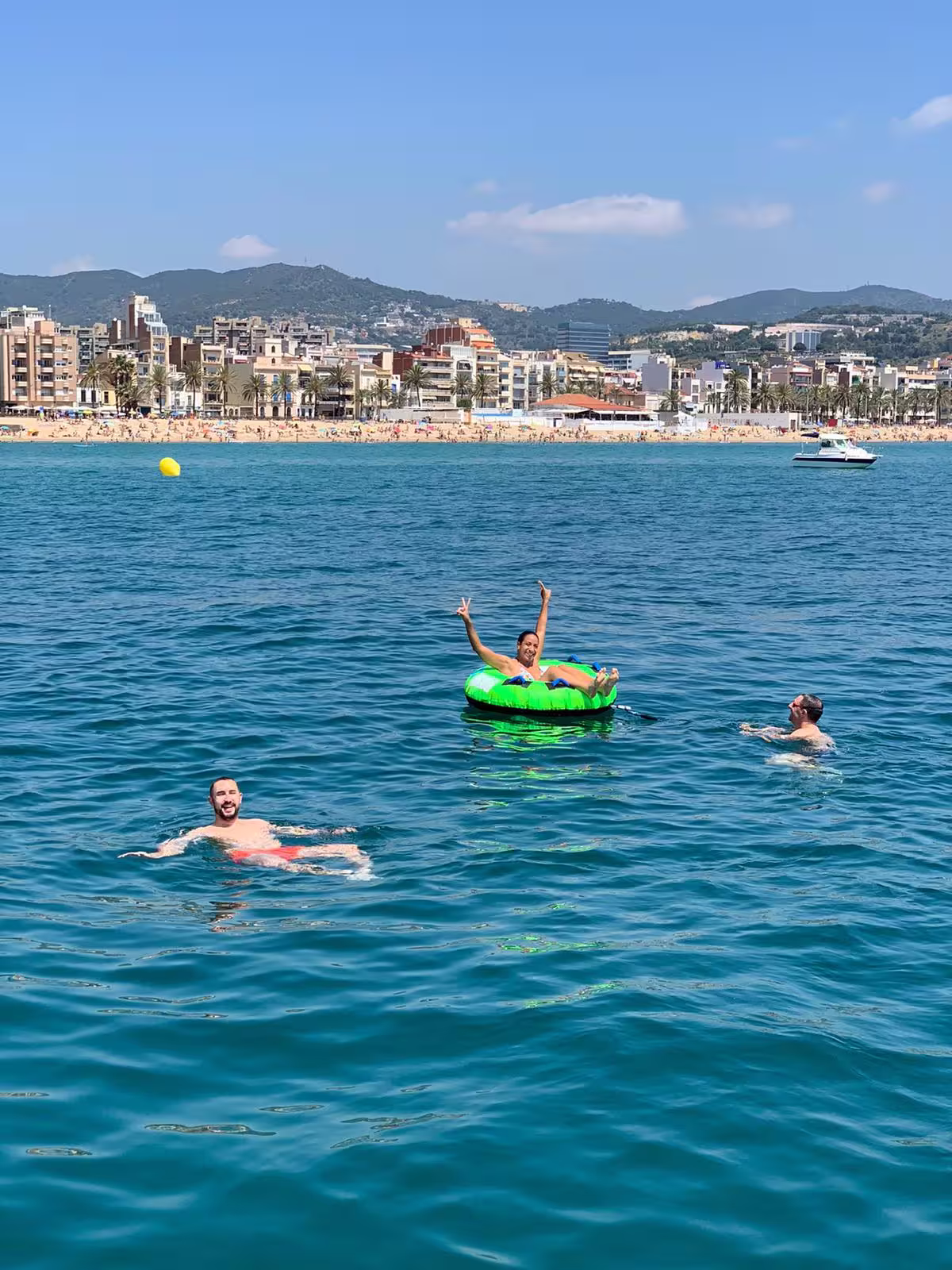 People enjoying a sunny day swimming near a vibrant Barcelona beach with a scenic city and mountain backdrop, ideal for sailing tours.