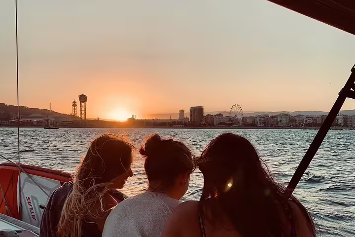 Three people enjoy a scenic sunset view of Barcelona's skyline from a sailboat, perfect for a small group tour with cava and snacks.